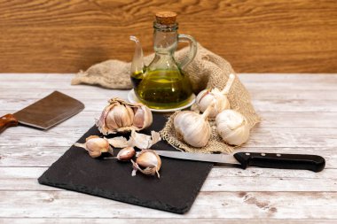 Tahta masadaki şişe bardağında olgun, çiğ sarımsak ve sarımsak yağı, çuval bezi, alternatif tıp ve organik temizleyici seçici odak ile.