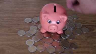 Kriz ve ekonomik konsept için para biriktirmeye çalışan bir adamın pembe seramik bir domuzcuğa bozuk para yerleştirdiği video..