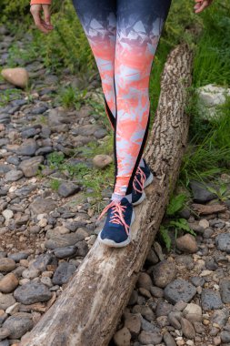 Gün batımında devrilmiş bir ağaç dalında dengede duran genç bir kızın bacaklarının ayrıntıları.