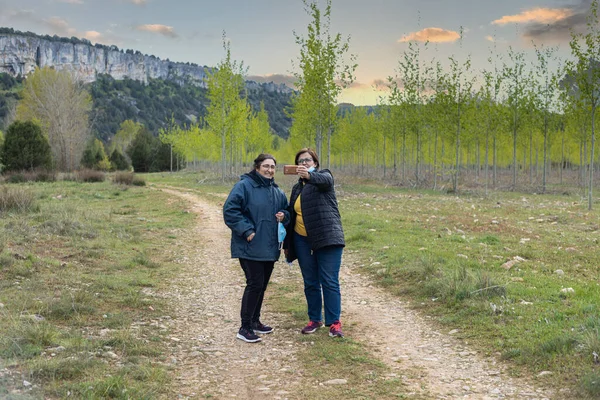 两名戴面具的中年女性朋友在日落时分徒步旅行时 带着智能手机的自拍作为纪念品 带着选择的焦点 远离了遮掩保护 — 图库照片