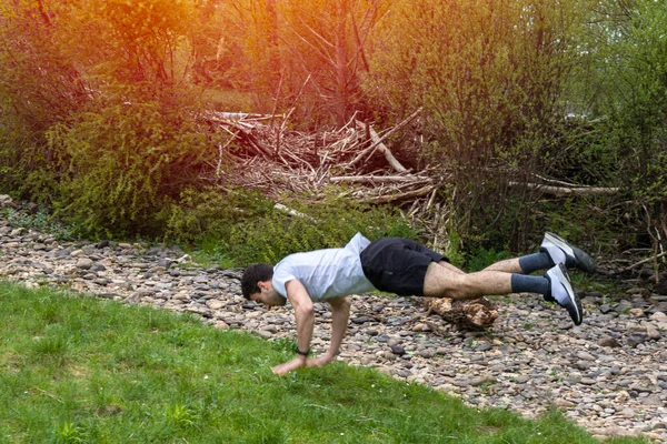 Spor giyim sektöründe genç bir kız, gün batımında gün batımında seçici bir odak noktasıyla güneşin ışınlarıyla şınav çekerek ve zıplayarak spor yapıyor..