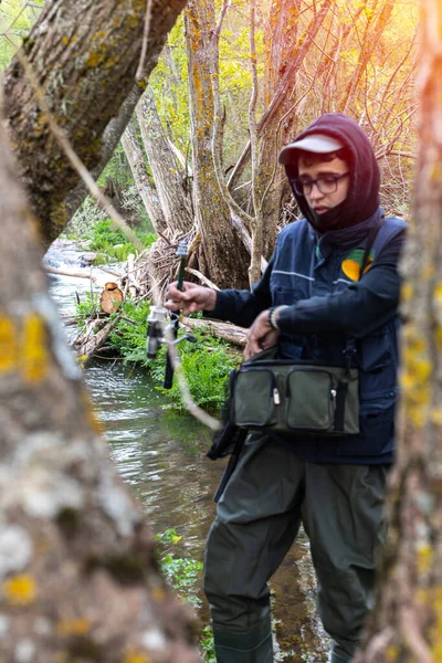 有一张冷酷脸的少年在河里钓鱼 河里有一根横穿溪流的钓竿 树上有选择的重点 — 图库照片