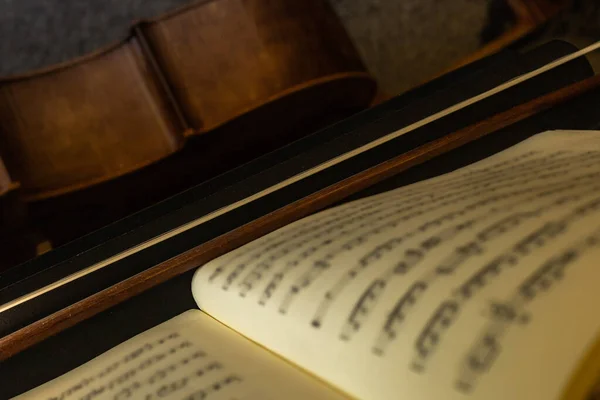 Selective focus of a music score supported on a music stand together with a musical bow and a wooden cello prior to a performance of the work.