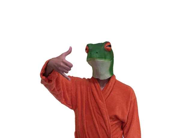 緑のカエルの動物のマスクを身に着けている若いですオレンジ色のバスローブとともにサーフィンハンドジェスチャーピンクと親指で白い背景に概念的なコピースペース — ストック写真