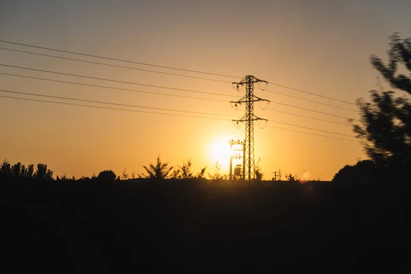 Yüksek voltaj kulesi günbatımı manzarasında elektrik iletmek için sarımsı güneş ve seçici odaklı.
