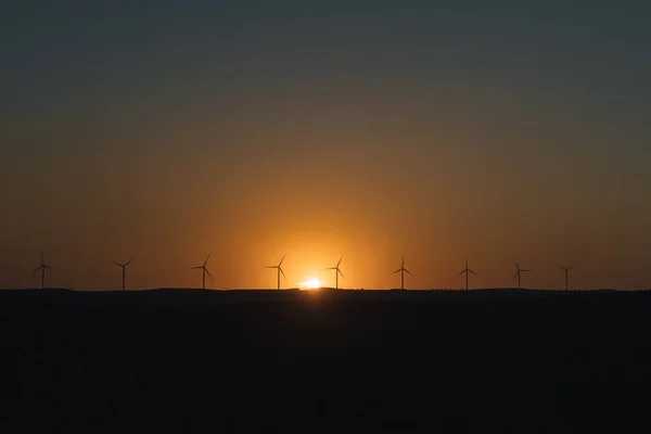 Gün batımında yel değirmenlerinin çizgisi seçici odaklı, sarımsı bir arka plan ışığı yaratıyor temiz yenilenebilir enerji ekolojisi