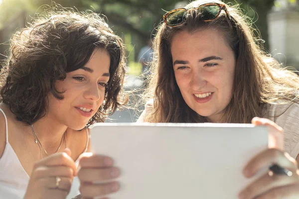 Danışmanlık yaparken, oyun oynarken veya güneşli bir günde selfie çekerken gülümseyen ve tabletin keyfini çıkaran iki genç insan.