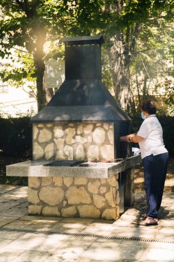 Kadın et pişirmek ve güneşli bir günü arkadaşlarıyla paylaşmak için şömineli bir barbekü hazırlıyor.