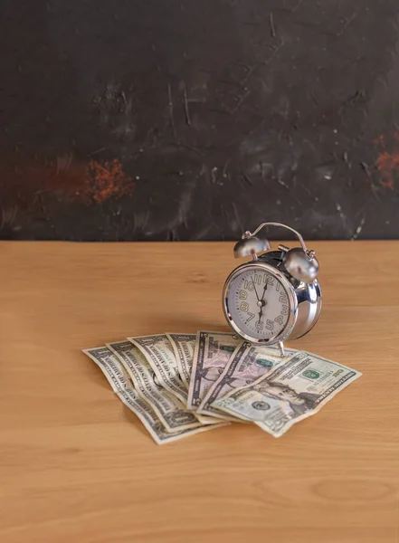 Dinero de diferentes tipos de dólares sobre la mesa y un reloj analógico que indica la hora y el concepto de economía del tiempo — Foto de Stock