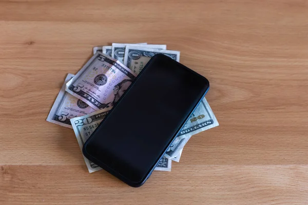 Teléfono móvil inteligente colocado en la parte superior del dinero de la factura del dólar en una mesa — Foto de Stock