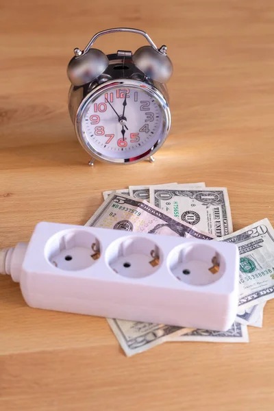 Cable de extensión con diferentes enchufes de luz colocados en dinero factura dólar con un reloj que indica la hora — Foto de Stock