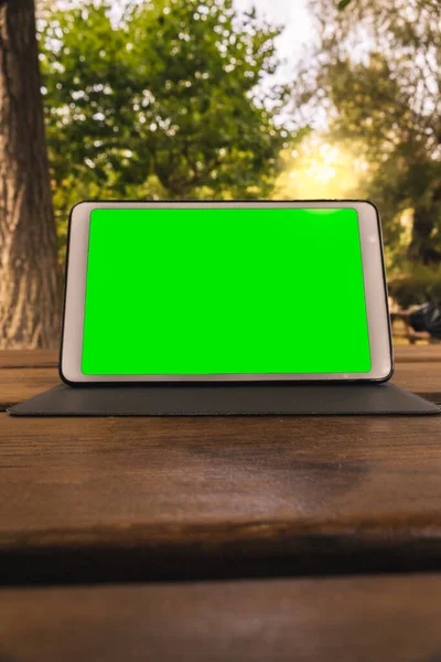 Tablette sur une table en bois dans un jardin avec un écran propre en vert chromé pour la publicité — Photo