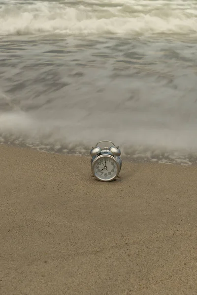 Vertical photo of an analog clock on the shore of the beach with the silky waves at dawn — Stock Photo, Image