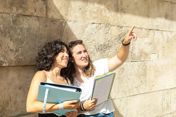 Dos jóvenes universitarias contemplando un monumento con cuaderno y carpeta para tomar notas de la guía —  Fotos de Stock