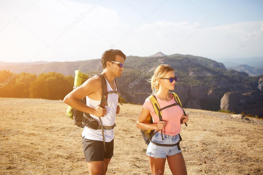Two travelers in sunglasses are resting after walking in mountains during their weekend