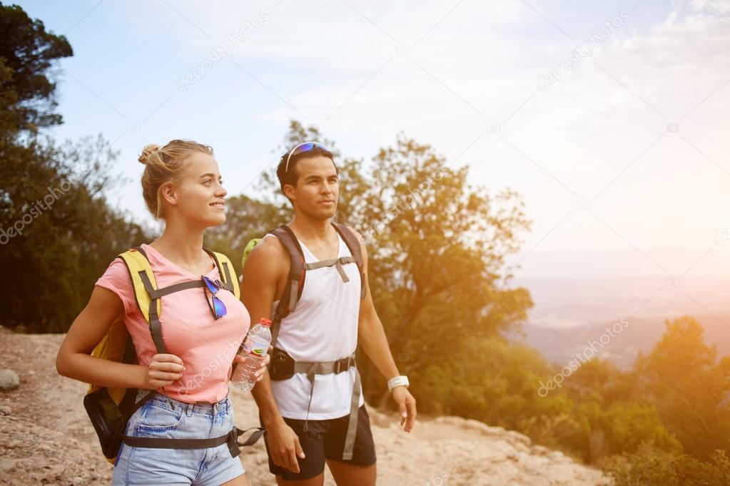 Man and woman with backpacks are looking away while are resting after walking in the fresh air outdoors