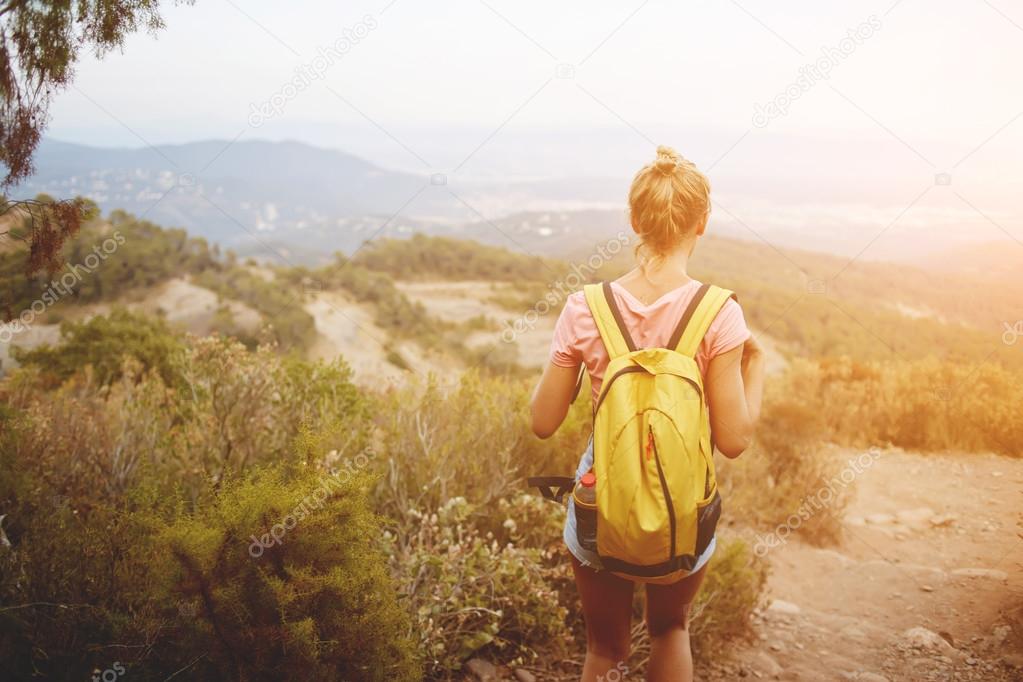 Blonde female wanderer is looking away while is standing on a high mountain in warm summer day