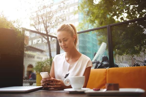 Жінка спілкується зі своїми друзями на мобільному телефоні, поки вона чекає свого замовлення в кафе — стокове фото