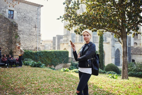 Young attractive female traveler is using cell telephone during break between excursion — Zdjęcie stockowe