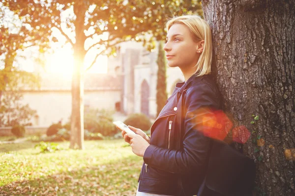 Thoughtful woman tourist is holding smart phone, while is enjoying free time in vacation — Stock Photo, Image