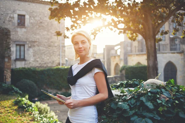 Charming woman is holding portable touch pad, while is standing in the park — Stock Photo, Image