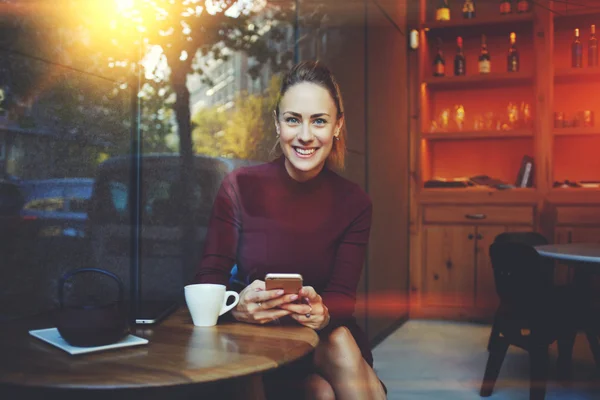 Wunderschöne fröhliche Frau plaudert mit ihren Freunden per Handy während der Pause im gemütlichen Café — Stockfoto