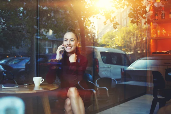 Gadis hipster muda menelepon dengan ponsel sambil duduk di kedai kopi kontemporer — Stok Foto
