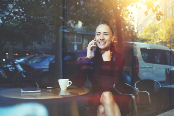Молодая веселая женщина звонит с мобильного телефона, сидя в кафе — стоковое фото