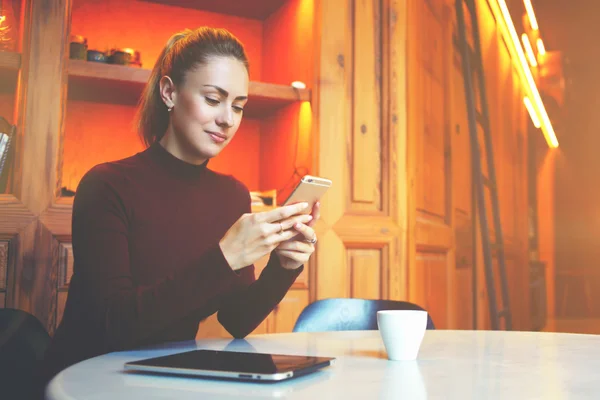 Preciosa mujer caucásica usando el teléfono celular mientras descansa en la cafetería durante las vacaciones de invierno — Foto de Stock