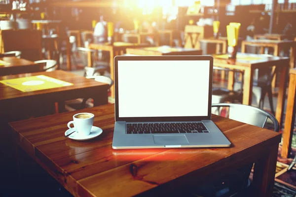 Computadora portátil abierta y taza de café acostado en una mesa de madera en el interior de la barra de café — Foto de Stock