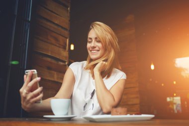 Kafede otururken cep telefon kendi kendine portre yapmak çekici gülümseyen hippi kız 