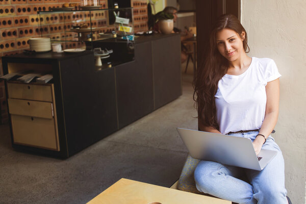 Gorgeous female freelancer using net-book for distance job while sitting in modern coffee shop