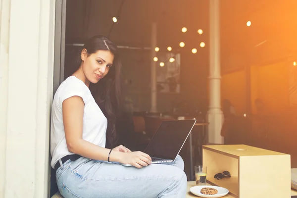 Female freelancer is using net-book for remote job while sitting in modern sidewalk coffee shop — Stock Photo, Image