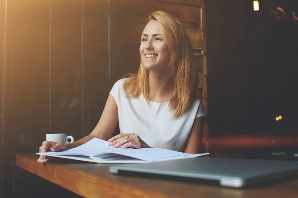 Schöne Frau mit süßem Lächeln, die wegschaut, während sie sich nach der Arbeit auf ihrem Laptop entspannt — Stockfoto
