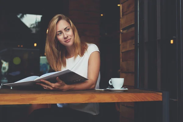 Chica hipster reflexivo mirando hacia otro lado mientras se relaja con la revista en el bar durante el tiempo de recreación — Foto de Stock