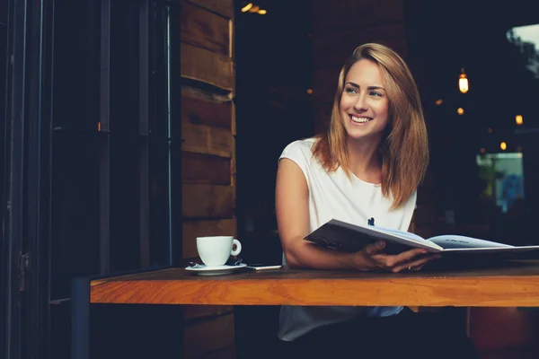 Feliz chica hipster sonriente disfrutando de un buen día mientras se relaja en el acogedor bar cafetería después del día de trabajo —  Fotos de Stock