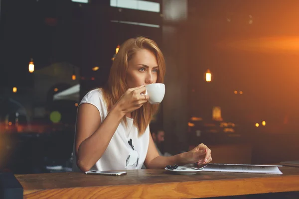 Femeia visătoare care se bucură de ceașcă de ceai în timp ce stă într-o cafenea confortabilă în timpul timpului ei de recreere — Fotografie, imagine de stoc