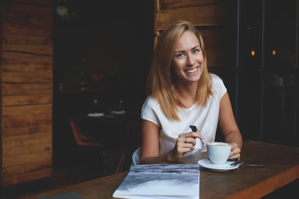 Alegre mujer caucásica con hermosa sonrisa disfrutando de su tiempo de recreación en el acogedor bar cafetería — Foto de Stock