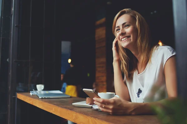Encantadora menina hipster sorridente recebeu boas notícias no telefone celular enquanto ela está sentada no aconchegante café — Fotografia de Stock