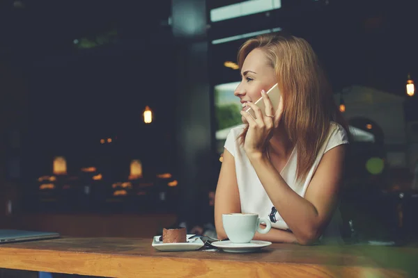 Sjarmerende dame med vakkert smil som snakker i mobiltelefon mens hun sitter på kafe i lunsjen – stockfoto