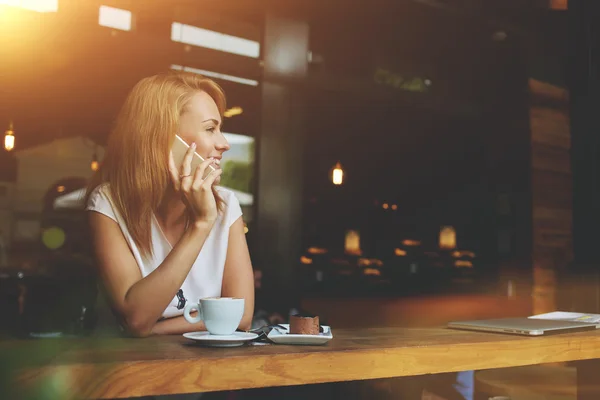 Wanita menawan dengan senyum indah berbicara di telepon seluler saat duduk di kafe saat makan siang — Stok Foto