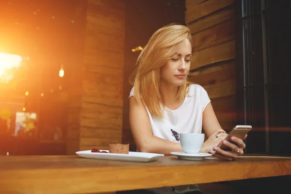 Gyönyörű csípő lány néz video-ra sejt telefon, közben reggeli reggeli a kávézó — Stock Fotó