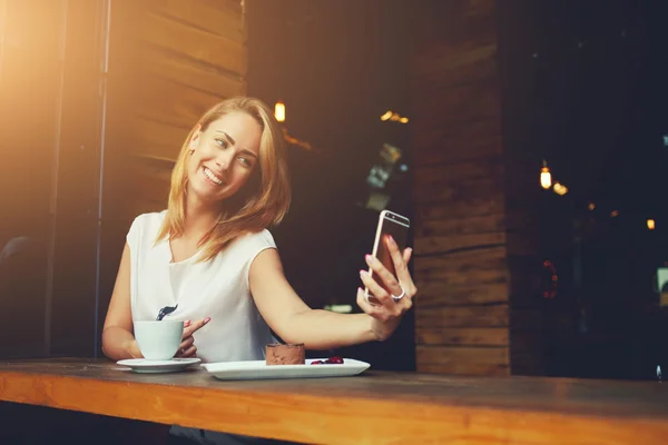 Szép nő aranyos mosollyal, hogy saját fotó neki szúró telefon alatt pihenő kávézó — Stock Fotó