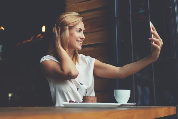 Menina hipster feliz fazendo foto com telefone celular para um bate-papo com amigos enquanto sentado no café — Fotografia de Stock