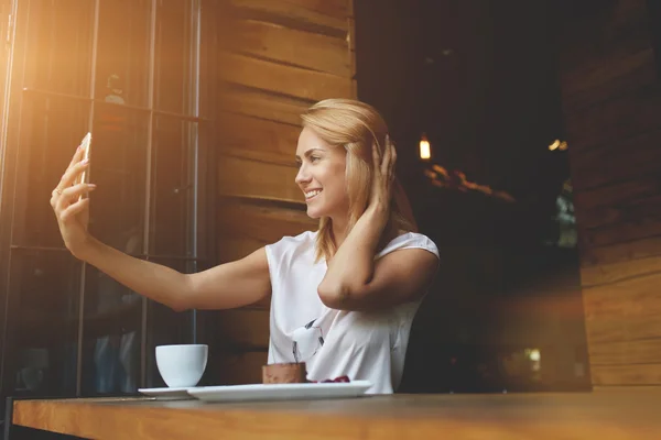 Menina hipster feliz fazendo foto com telefone celular para um bate-papo com amigos enquanto sentado no café — Fotografia de Stock