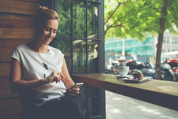 Glückliche Kaukasierin, die ihre Fotos auf dem Handy anschaut, während sie sich in der Freizeit im Café entspannen — Stockfoto