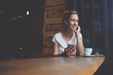 Mutlu Avrupalı kadın iş gününden sonra modern kahve dükkanında dinlenirken cep telefonu kullanarak