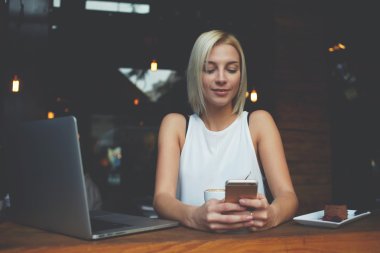 Young hipster girl using cell telephone while enjoying her free time after work on net-book 
