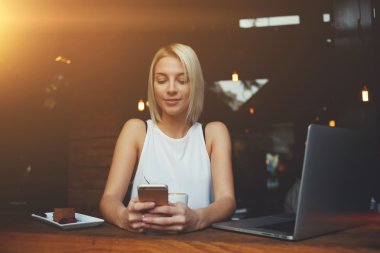 Young hipster girl using cell telephone while enjoying her free time after work on net-book 