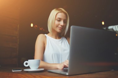 Woman freelancer is working on laptop computer during breakfast in cafe bar 